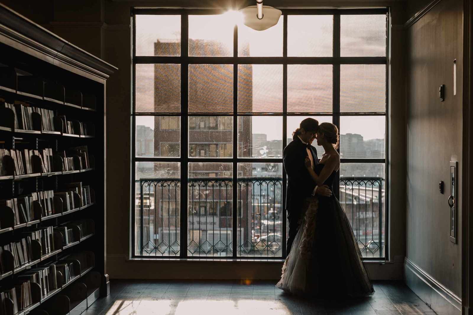 A bride and groom touching heads in front of a big window at the Nashville Public Library